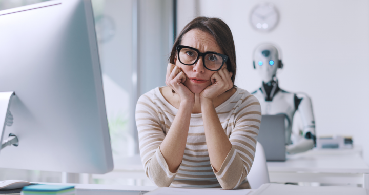 Mitarbeiterin sitzt unsicher vor dem Computer, im Hintergrund ein Roboter – Symbol für Unsicherheit im Umgang mit KI im Büroalltag